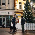 Text: "Grape Tree" und "MOBILES & VAPES". Zwei Männer mit Hunden vor einem geschmückten Weihnachtsbaum und Lichterketten.