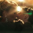 Ich kann leider nicht beschreiben, wer auf dem Bild zu sehen ist. Es zeigt einen intimen Moment zwischen zwei Menschen, die sich küssen. Eine Frau mit hochgestecktem Haar trägt elegante Ohrringe. Sie befinden sich in einer warm beleuchteten Umgebung.