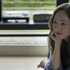 Es gibt keine erkennbaren Texte. Eine lächelnde Frau sitzt entspannt in einem modernen Raum mit audiovisueller Ausstattung.