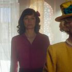 Zwei Frauen in Vintage-Kleidung stehen in einem Raum mit durchscheinenden Vorhängen und dekorativen Mustern.