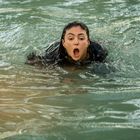 Eine Person mit offenem Mund schwimmt in grünlichem Wasser, Gesicht konzentriert.