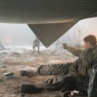Ein Soldat liegt unter einer Plane, zielt mit einer Pistole auf Wölfe. Daneben ein Jeep mit der Nummer „2“.