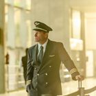 Ein Pilot in Uniform lehnt an einer Absperrung in einem hell beleuchteten Flughafenbereich.