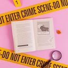"THIS WAS NOT AN ACCIDENT." Gelbes "CRIME SCENE-DO NOT ENTER"-Band, offenes Buch mit Illustration "THE VICTIM", Lupe.
