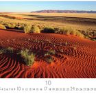 "Düne aus rotem Sand" steht am unteren Rand. Vorne rote Dünen mit Grasbüscheln, hinten weite Wüstenlandschaft und Berge.