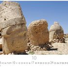"Nemrut Dagi" und "10 CASARES EDITION". Zerbrochene Steinköpfe vor klarem Himmel, staubige Landschaft.