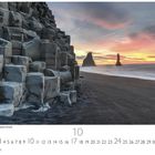 Reynisdrangar am Reynisfjara Strand. Vorne Basaltfelsen, dahinter schwarze Sandküste mit Meer und zwei markanten Felsnadeln im Wasser.