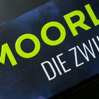 Der Text "MOORLAND" ist in großer, gelber Schrift, darunter "DIE ZWILLINGE" in weiß. Hintergrund in dunklen Tönen.