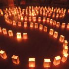 Leuchtende Papierlaternen bilden eine spiralförmige Anordnung auf einem Holzboden in einem abgedunkelten Raum.