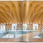 Ein modernes Holzgebäude mit geometrischem Dach, großen Fenstern und Personen, die einen weiten Raum erkunden.
