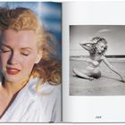Auf der rechten Seite steht "265". Links eine Frau mit blonden Locken in einem Bademantel, Augen geschlossen. Rechts am Strand.