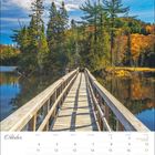 "Oktober" Kalender mit Tagen und Feiertagen. Holzbrücke führt durch farbenfrohe Herbstlandschaft aus Bäumen und See.
