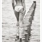 Text: "Oktober" und Kalenderdaten darunter.  
Beschreibung: Eine Frau in Unterwäsche und Stiefeln geht auf Pfählen ins Wasser.