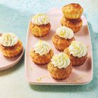 Zitronen-Muffins mit Sahnetopping und Zitronenzesten auf rosa Tellern auf hellblauem Untergrund.