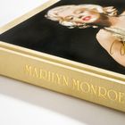 „MARILYN MONROE 100“ in Gold auf cremefarbenem Leinen aufgedruckt. Cover zeigt lächelnde Frau in goldener Kleidung.