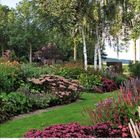 "11" und Kalenderdaten darunter. Eine Gartenlandschaft mit zwei Bänken, umgeben von üppiger Vegetation und Herbstlaub.