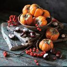 Ein Kalenderblatt mit der Zahl "10" für Oktober 2024. Eine Schale mit orangefarbenen Kakis und Kastanien auf Holz.