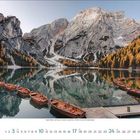 Oktober 2023 Kalender,  Bild eines Sees mit Ruderbooten, umgeben von Bergen und herbstlichen Bäumen, auf einem Steg.