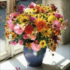 Bunter Blumenstrauß in blauer Vase vor einem Fenster, mit Sonnenlicht beleuchtet.