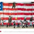 Ein bunt bemalter Wand mit amerikanischer Flagge, darauf stehen Menschen. Der Text lautet: "What we do in life echoes in eternity."