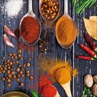 Verschiedene Gewürze wie Chili, Pfeffer, Kurkuma und Kräuter auf Löffeln und verstreut auf hölzernem Untergrund.