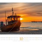 Kalender mit Oktober, Feiertagen und einem Fischerboot „SEETEUFEL“ bei Sonnenuntergang am Strand.