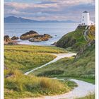 Zitat von Mark Twain über die Vorteile des Reisens. Ein Leuchtturm auf einem grasbewachsenen Hügel an der Küste.