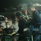 Männer und Frauen in Uniformen, viele mit Masken. Ein Mann hält ein kleines Kind. Im Hintergrund ein Krankenwagen.