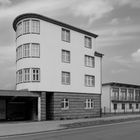 Graffiti in einem offenen, überdachten Bereich. Modernes Gebäude mit Rundung, daneben ein langer, flacher Bau.