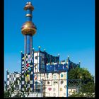 Kalenderseite mit Zahlen 1 bis 31 und „X 2027“. Architektur mit buntem, künstlerischem Design und goldenen Kugeln.