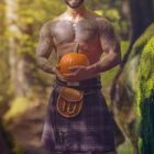 Text: "OKTOBER" mit einem Kalendarium unten. Ein Mann in einem Kilt hält einen Kürbis, lächelt in einem Wald.