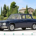 Alfa Romeo Giulia 1600 Ti Super Baujahr 1972. Ein blauer Oldtimer vor einem steinernen Gebäude und grünen Bäumen.