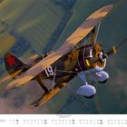 Text: "OKTOBER", Zahlen 1-31 darunter aufgelistet. Ein Doppeldecker-Flugzeug mit roten Sternen fliegt über einer Landschaft.