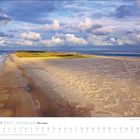 Oktober 2027 | Küstenland. Ein weiter Sandstrand neben blauem Meer und grünen Dünen unter bewölktem Himmel.