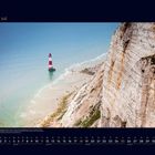 07 Juli. Kalender mit Leuchtturmbild, am Meer mit hohen Klippen. Sandiger Strand im Vordergrund.