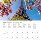 Kalender für März 2027 mit mehrsprachigen Wochentagen. Oben der Eiffelturm, umrahmt von blühenden rosa Zweigen.
