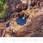 Kalenderseite für Oktober; Luftaufnahme eines Wasserfalls, der in ein rundes Becken fließt, umgeben von Felsen und Bäumen.