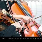 Kalenderseite: Zahlen 1-31, Monat 10 hervorgehoben. Gezeigt sind Hände, die Cello und Geige spielen.
