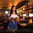 Kalendertage vom 01. bis 31., mit Wochentagen darunter. Eine Frau trägt ein traditionelles Dirndl und hält zwei Bierkrüge.