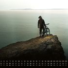 Kalender mit Novembertagen. Person mit Fahrrad auf Klippe, blickt aufs Meer. Ruhige, weite Wasserlandschaft.