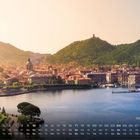 "Comersee 10" unten rechts; Kalenderleiste über Panorama einer Stadt am See mit Hügeln im Hintergrund, warmes Licht.