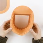 Zwei Hände halten ein gefaltetes, orangenes Papierobjekt mit gezackten Kanten, auf einem weißen Hintergrund.