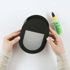 "Bastelkleber", "Hobby Glue" steht auf einer Klebeflasche. Zwei Hände halten ein schwarzes, ovales Objekt mit grauer Fläche.