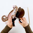 Es gibt keinen Text. Zwei Hände basteln eine Affenlaterne aus Papier mit einer Zange.
