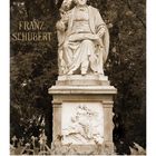 Text: Franz Schubert, Casares Edition. Eine Statue von Schubert sitzt inmitten von Bäumen, darunter Reliefkunst.