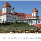Kurhaus Binz. Elegantes Gebäude mit weißen und gelben Fassaden, roten Dächern, umgeben von Strandkörben im Vordergrund.
