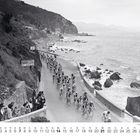 "CALZE AMBROSIANA" auf einem Banner. Radrennen entlang einer Küstenstraße mit Zuschauern und Wellen im Hintergrund.