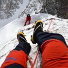 Eisiger Bergstieg; roter Kletterer und Kletterseil von oben betrachtet. Person trägt orange Hose, gelbe Klettersteigeisen.