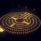 Leuchtendes Kerzenlabyrinth in der Dunkelheit mit spiralförmigem Muster auf dem Boden.