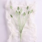 Zarte grüne Blätter aus Garn auf zerknittertem, weißem Hintergrund, leicht angeordnet wie ein Blumenstrauß.
